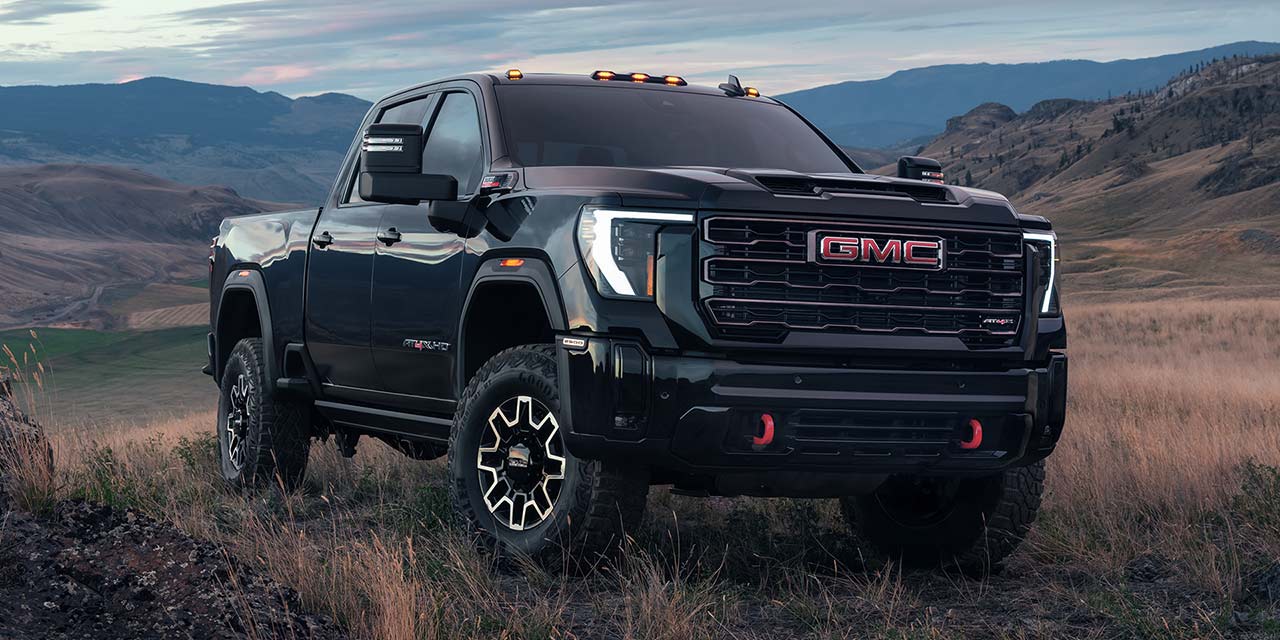 Front Three-Quarters View of a 2026 GMC Sierra HD Parked on a Terrain Field Surrounded by Mountains