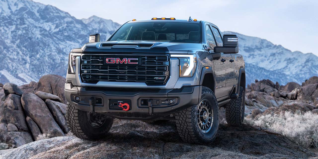 Wide Front Three-Quarters View of a 2026 GMC Sierra HD AT4 Truck Parked in Front of Snow-Covered Mountains