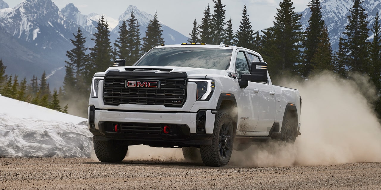 Front Three-Quarters View of a White 2026 GMC Sierra HD AT4 Heavy Duty Off-Road Truck Driving Through the Mountains Kicking Up Dirt