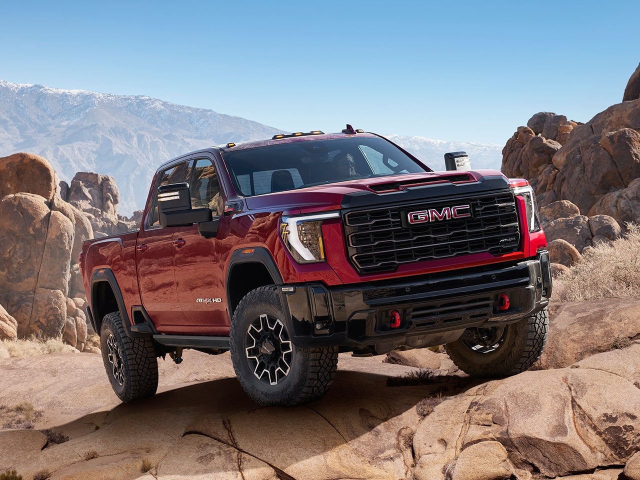 Wide Front Three-Quarters View of a 2026 GMC Sierra HD AT4 Heavy Duty Off-Road Truck Driving Through the Mountains