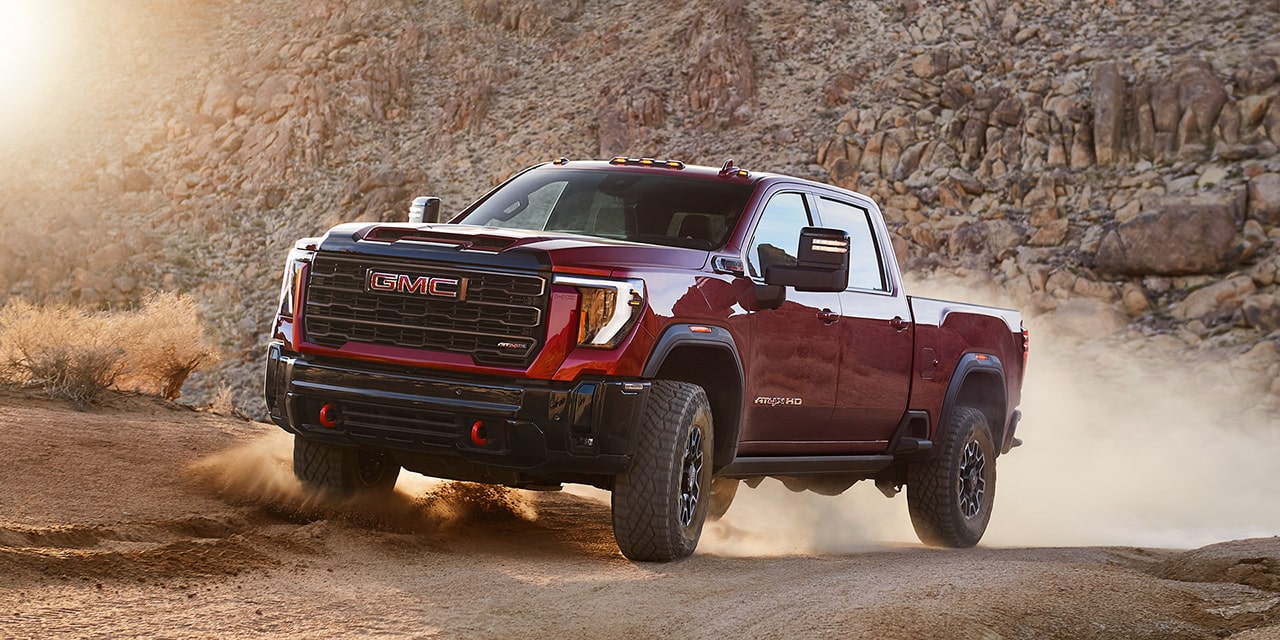 Wide Front Three-Quarters View of a 2026 GMC Sierra HD AT4 Heavy Duty Off-Road Truck Driving Through the Mountains