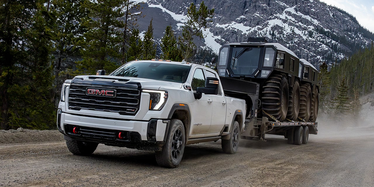 The 2026 GMC Sierra HD Heavy Duty Truck Pulling a Trailer Down a Dirt Road Lined with Pine Trees