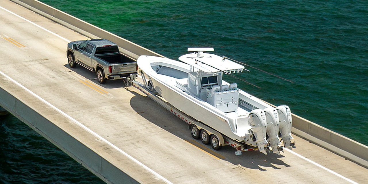 Wide Rear Three-Quarters Birdseye View of a 2026 GMC Sierra HD Hauling a Boat on an Open Road Near a Lake