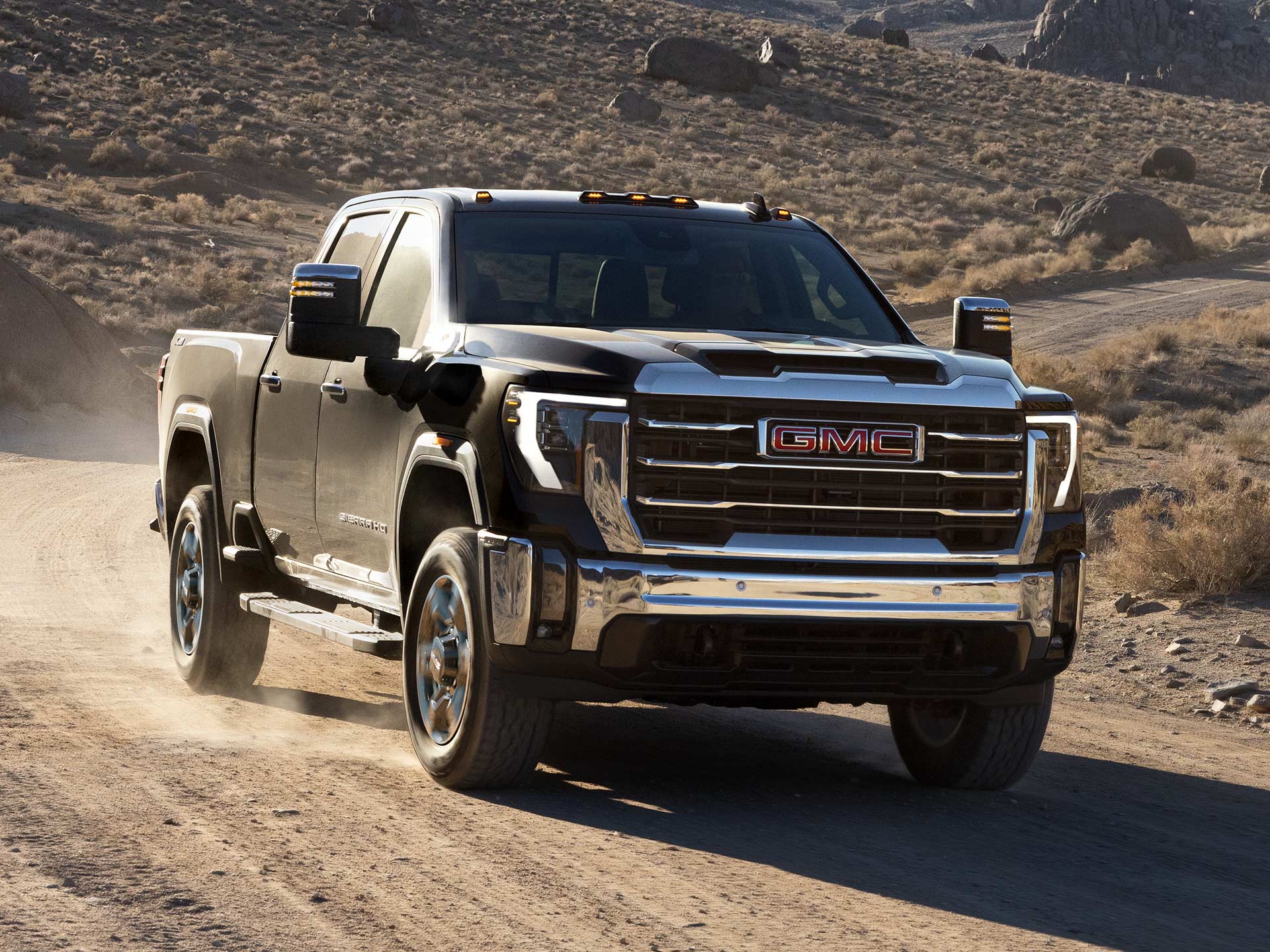 Front Three-Quarter View of the 2026 GMC Sierra HD Heavy Duty Truck Driving Down a Dirt Road