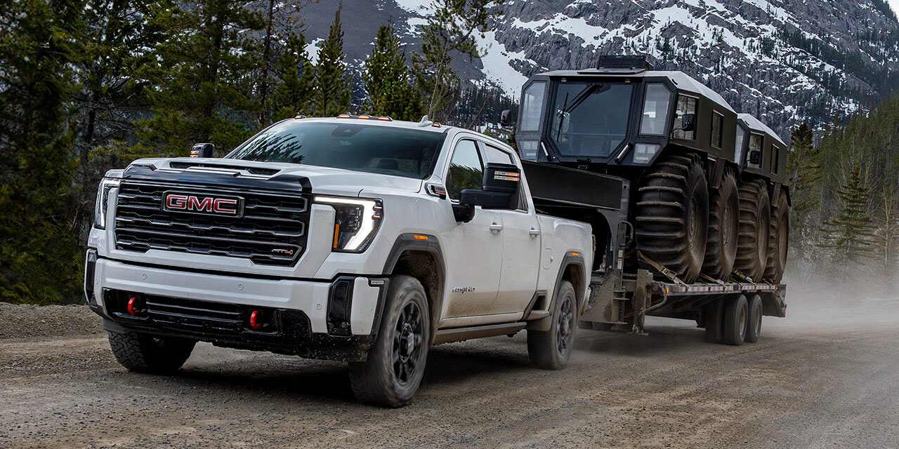 The 2026 GMC Sierra HD Heavy Duty Truck Pulling a Trailer Down a Dirt Road Lined with Pine Trees