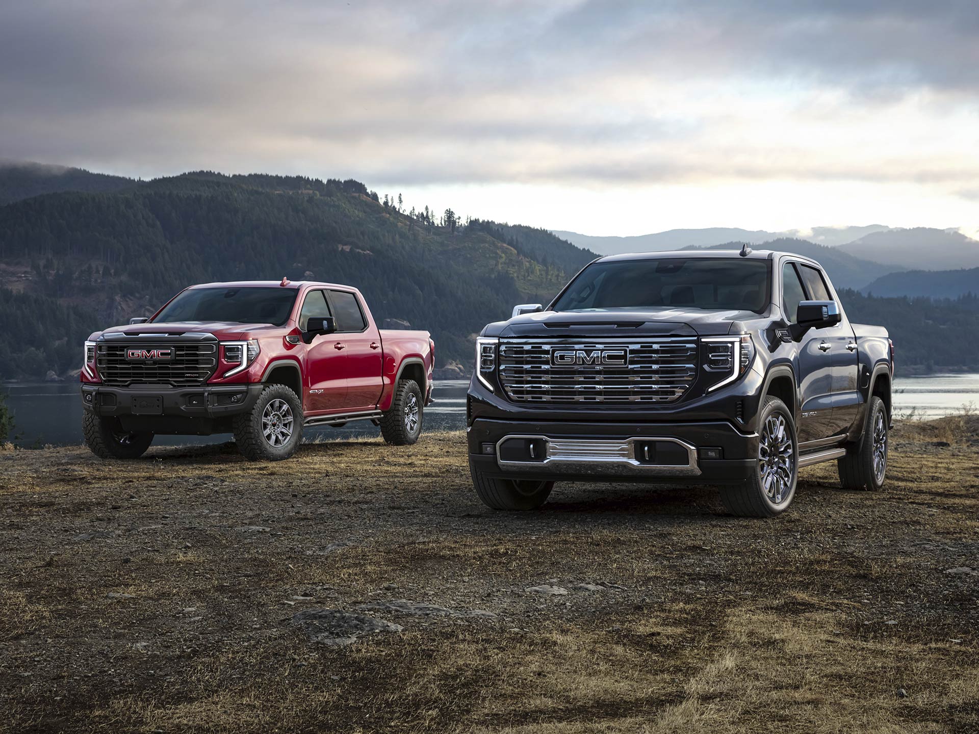 Front View of Two 2026 GMC Sierra 1500 Pickup Trucks Parked in a Grassy Field by a Body of Water