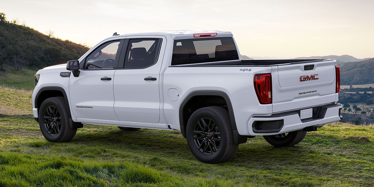 Rear Three-Quarters View of a White 2026 GMC Sierra Pickup Truck Parked in a Grassy Field