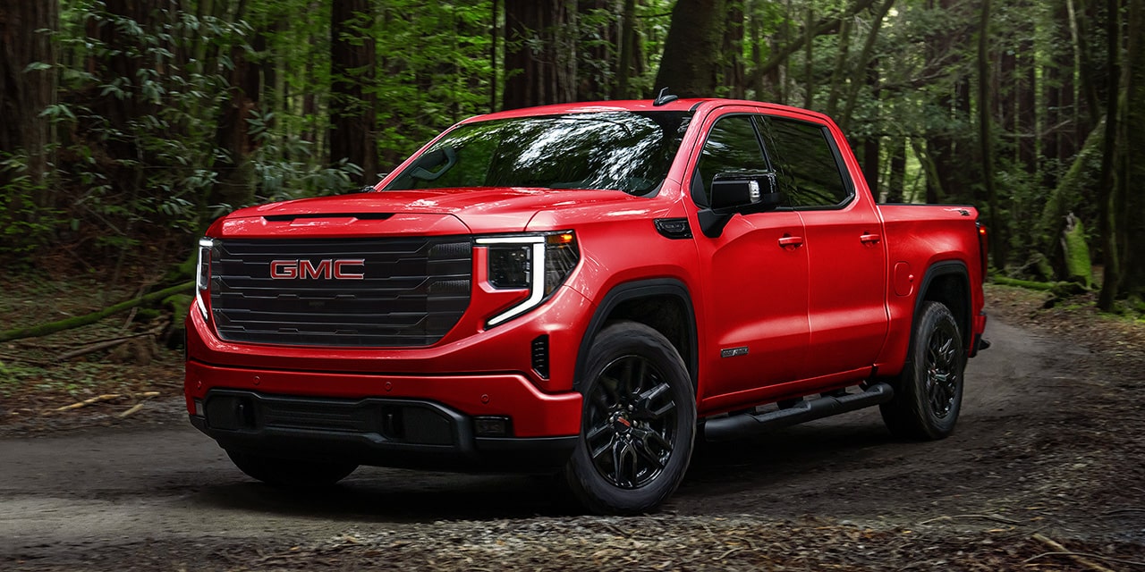 Front Three-Quarters View of a Red 2026 GMC Sierra 1500 Pickup Truck Parked in a Green Forest