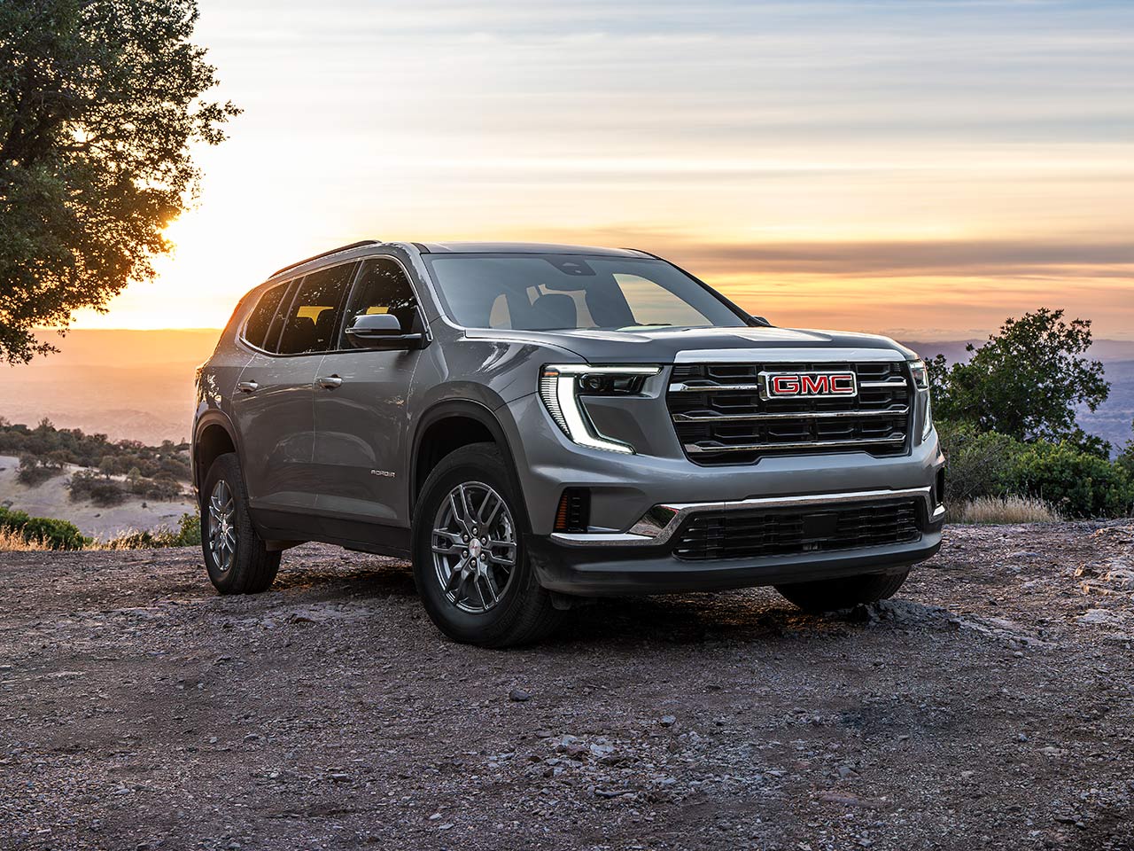 Front Three-Quarters View of the GMC Acadia Parked On a Hillside With A Sunset In the Distance