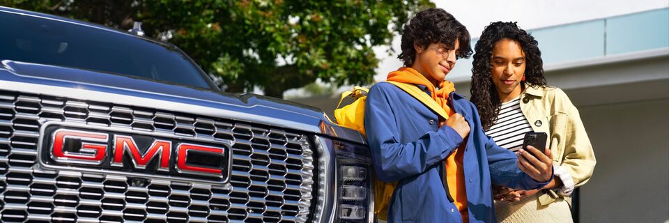 Two People Standing Next to the Front of a GMC Vehicle Looking at a Smartphone