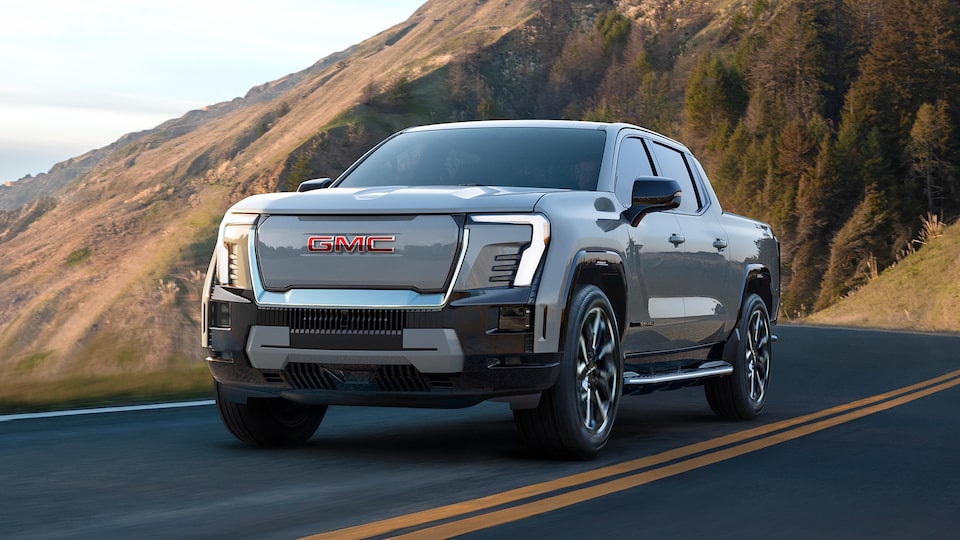 Three-quarters View of a 2026 GMC Sierra EV Pickup Truck Driving Through a Mountain Road