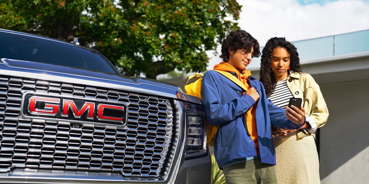 Two People Standing Next to the Front of a GMC Vehicle Looking at a Smartphone