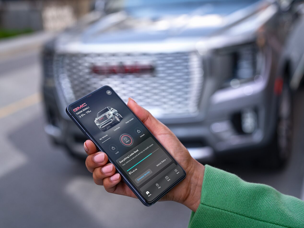 Close-up of a Smartphone Displaying the myGMC App with a GMC Vehicle Parked in the Background