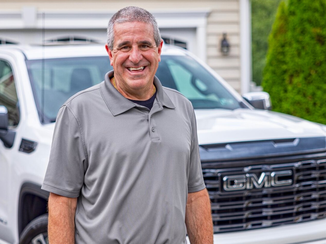 OnStar member Marco C. standing in front of his white GMC truck on a sunny day